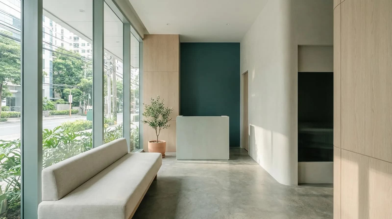 A quiet, daylit dental clinic reception with pale timber panelling, a deep teal accent wall and a linen bench beneath full-height windows